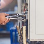 Technician using tools to repair an air conditioning unit, highlighting professional AC repair services for energy efficiency and safety.
