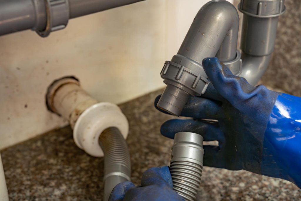 plumber repairing under sink pipes drain connection